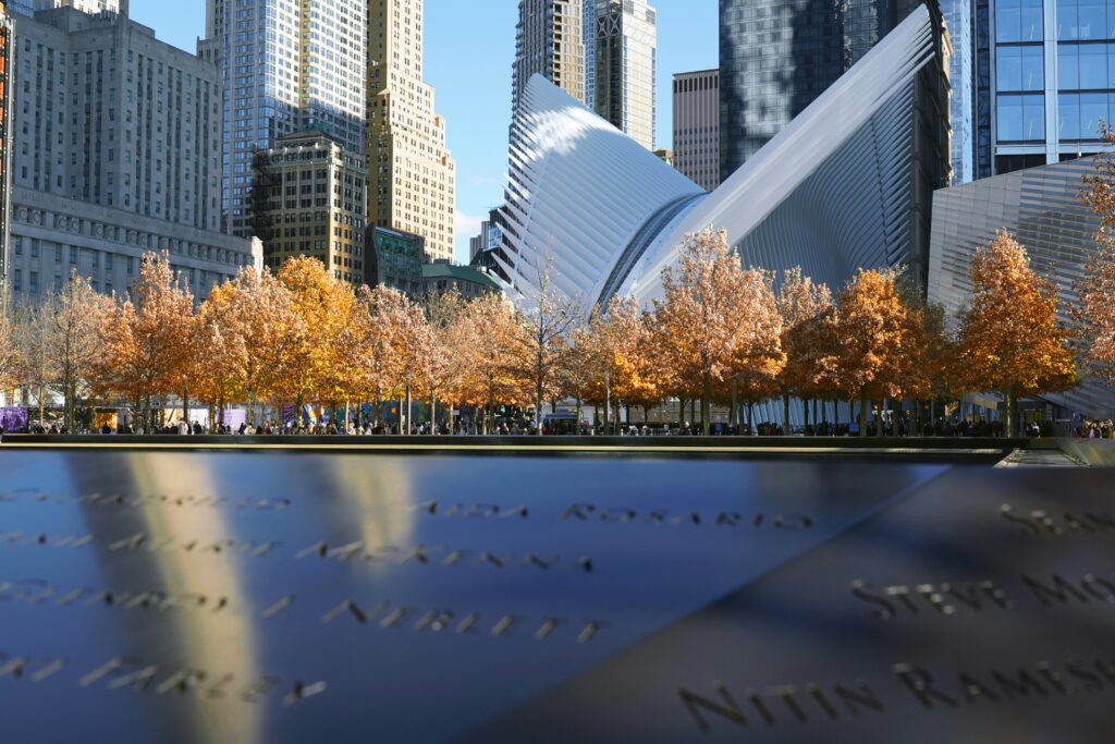 9/11 Memorial names with the World Trade Center Oculus and autumn trees in Lower Manhattan.